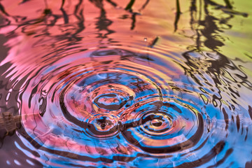 Raindrops fall on the surface of the water. The circles from the raindrops on the water surface. Abstract color background of circles on the water and falling drops.