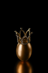  Golden egg in a crown on a black background with reflection. Close up, Copy space. Easter, diet,...
