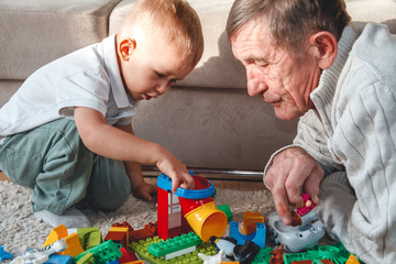 Elderly grandpa or grandfather plays with his little grandson