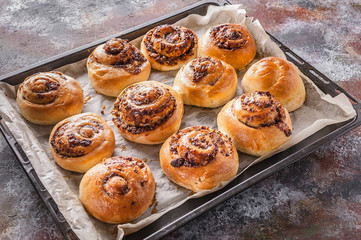 Fresh sweet homemade cinnamon rolls with chocolate cream on a baking sheet.