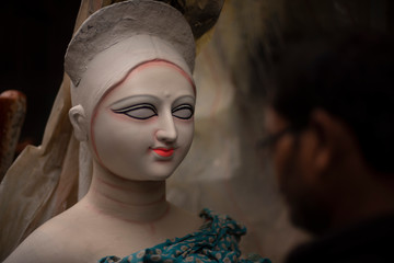 An Indian artist making and painting the eyes of clay idols of Hindu Goddess Saraswati for the Indian Bengali festival in winter in Bengal. Indian culture and religion.