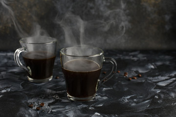 Two glass mugs of black freshly brewed coffee. Hot Coffee Steaming. Transparent cups on a dark background with coffee beans. Copy space