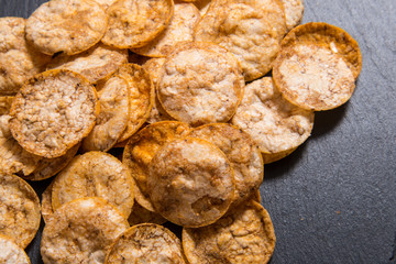 Top view pile of organic, crispy, baked, whole grain rice chips with spices. Gluten free healthy snack. On black sliced stone background
