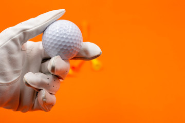 Golfer is holding golf ball in hand on orange background