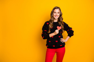 Photo of pretty curly lady amour holding little paper heart hear chest symbolizing cardiology health care wear hearts pattern sweater red trousers isolated yellow color background