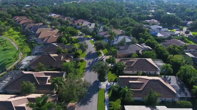 Aerial view gliding down the street above upscale tropical homes in gated community in 4K