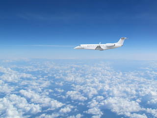 White private jet business jet flies against backdrop of beautiful white clouds on blue sky