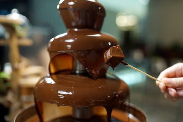 Homemade chocolate fountain fondue with marshmallow on a skewer dripping in chocolate sauce on...