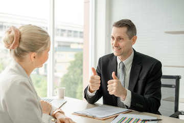 Boss Businessman doing thumbs up congratulation to woman employee at desk in office room