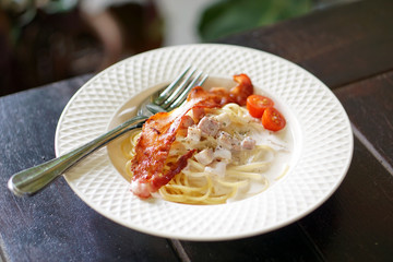 A plate of homemade spaghetti carbonara with ham and parmesan cheese on top with crispy bacon and fresh tomato.