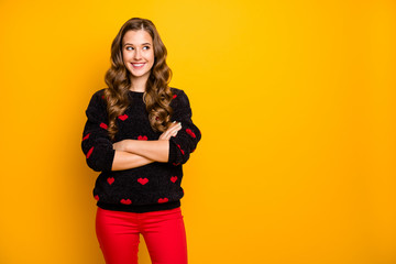 Photo of pretty curly long hairdo lady self-confidently crossing arms good mood look side empty space wear black red hearts pattern jumper trousers isolated yellow color background