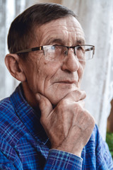 Senior standing at the window and thinking about something or fo