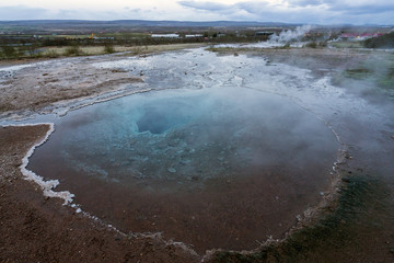 Clear hot pool with big hole towards the ground in the geysir and haukadalur area during blue hour and no people. Smoke from Strokkur and city light in the background. Icelandic traveling concept.