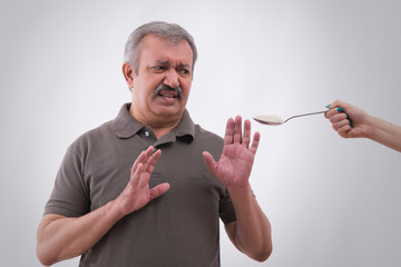 Portrait of a senior man looking at a spoonful of sugar.