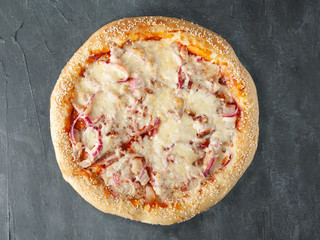 Homemade Pizza with ham and slices of bacon, mozzarella and parmesan cheeses, pickled red onions and tomato sauce. Wide side. View from above. On a gray concrete background. Isolated.