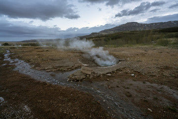 Litli-geysir or mini geysir next to Strokkur in Haukaalur area in the Icelandic countryside. Blue hour and cloudy sky with boiling hot pool infront. Travelin concept.