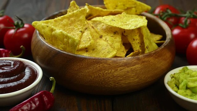 nachos lie in a wooden bowl a hand takes and dries nacho in sauce