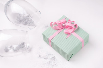 Gift in mint packaging on a white background next to glasses filled with sparkles. close-up