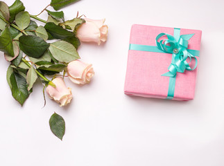 A gift in pink packaging on a white background next to a bouquet of white roses. there is a place for copy space