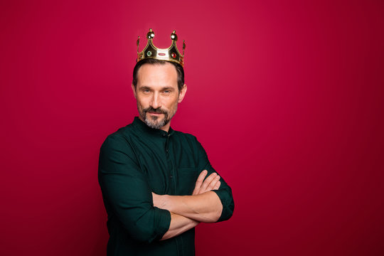 Turned photo of arrogant man looking at you with hands folded and crown on head isolated vivid color background