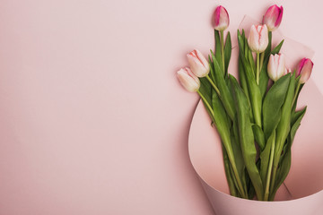 top view of pink and purple tulips wrapped in paper swirl on pink background
