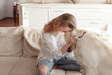 Young pretty woman in casual clothes hugging her beloved big white dog sitting on the sofa in the...