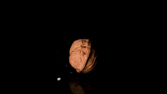 Cracking the walnut shell with a hummer in slow motion. Isolated on the black background on the reflective surface