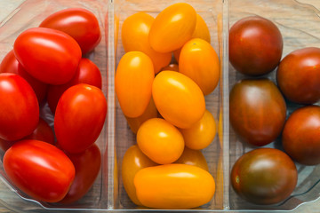 Cherry tomatoes in a plastic container, different varieties of yellow and red tomatoes