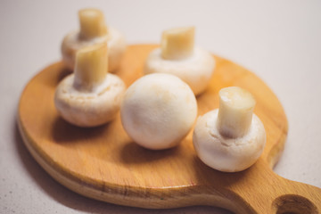 Five fresh champignons lie on a wooden board, side view.