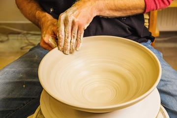 Potter master working on potter's wheel, making new bowl from raw clay, hands detail