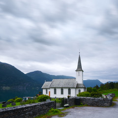 Fototapeta na wymiar Typical christianity church with cemetery of Nes village, parish church in Luster Municipality in Sogn og Fjordane county, Norway. Lustrafjorden fjord on background. Landscape photography