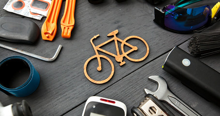 A lot of different bicycle accessories lying on wooden table around a little bicycle icon