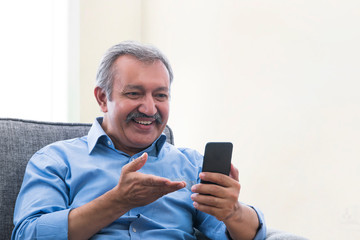Portrait of a senior man sitting at home and doing a video chat on phone.
