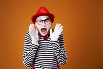 Surprised mime man in red hat and vest on orange background