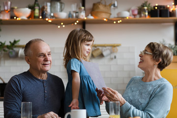 Happy middle-aged mature grandparents and child granddaughter having fun playing at home