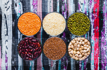 Set of different cereals and legumes in a glass bowls on background of colorful motley rug or carpet. Flat lay. Healthy nutrition food concept.