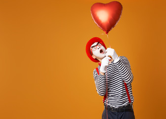 Mime in red hat and vest holds heart ball in his hands while looking up