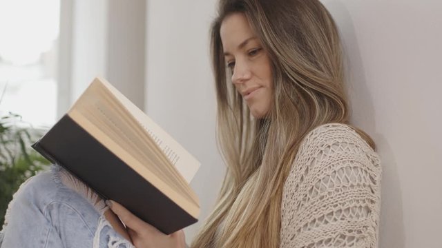 beautiful young woman reading a book, leaning on the wall. 4k slow motion, handheld
