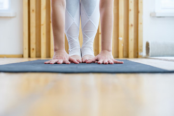 View of unidentified young athlete doing head to knees exercise uttanasana standing forward bend pose barefoot on floor in gym. Concept of regular training and healthy strong body. Advertising space