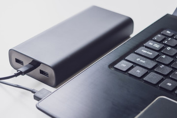An open laptop is charged using a power bank via a cable. Portable modern devices. External battery, cable, USB and laptop, close-up
