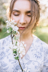 Fototapeta premium Portrait of young beautiful girl in white lace dress in apple garden, in the tree crown, fingers near mouth