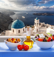 Greek salad against famous church in Thira town on Santorini island in Greece - obrazy, fototapety, plakaty