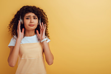 upset bi-racial girl listening music in headphones on yellow background