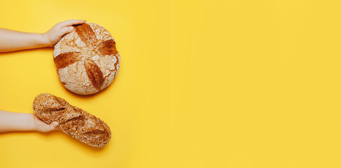 Tasty big round bread in child's hands on yellow background.