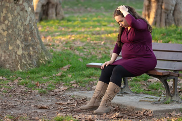 Naklejka na ściany i meble Sick young pregnant woman on a park bench