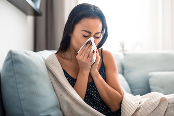 Asian girl suffering from cold sitting on bed at home