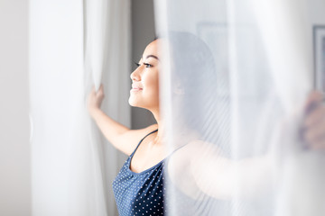 Asian girl wearing pajamas open window lace curtains in home at morning