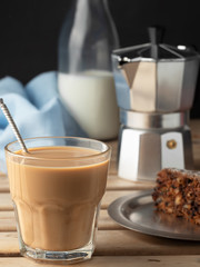 Glass with aromatic coffee with milk or latte. Plate with carrot cake on a wooden vintage table. Close-up, vertical orientation. Shallow depth of field. Breakfast or snack concept.