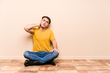 Young caucasian man sitting on the floor isolated touching back of head, thinking and making a choice.