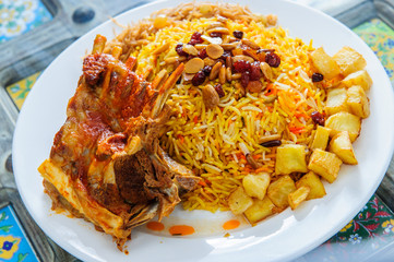 Plate of yellow rice topped with mutton meat and potatoes.